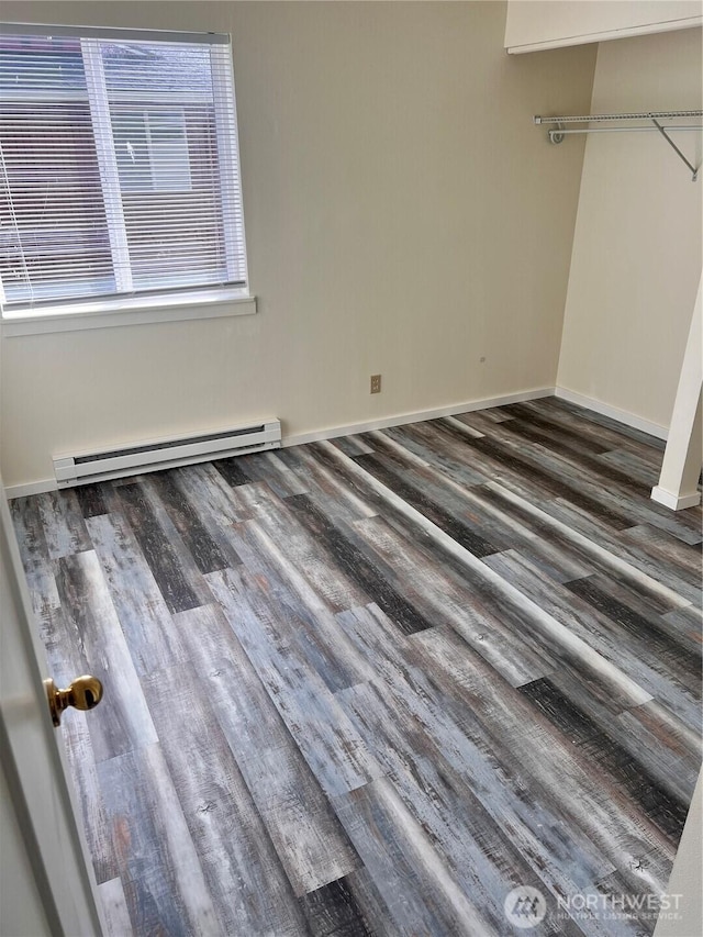 empty room featuring a baseboard heating unit, wood finished floors, and baseboards