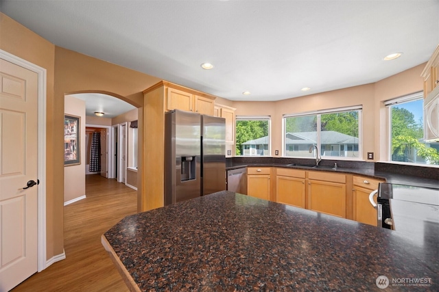kitchen featuring stainless steel appliances, a sink, arched walkways, wood finished floors, and light brown cabinets