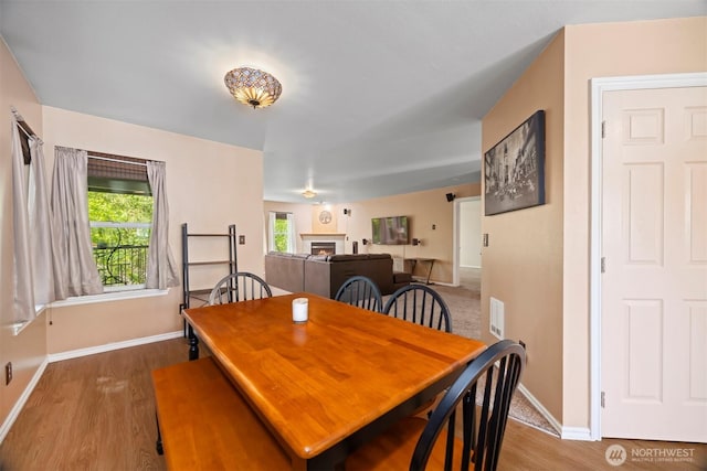 dining space with baseboards, wood finished floors, and a warm lit fireplace