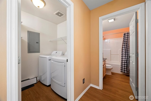 washroom with electric panel, a baseboard radiator, wood finished floors, and washing machine and clothes dryer