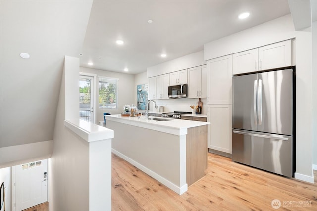 kitchen featuring light wood-style flooring, an island with sink, a sink, stainless steel appliances, and light countertops