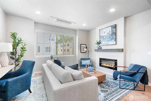 living room featuring recessed lighting, light wood-style floors, baseboards, and a glass covered fireplace