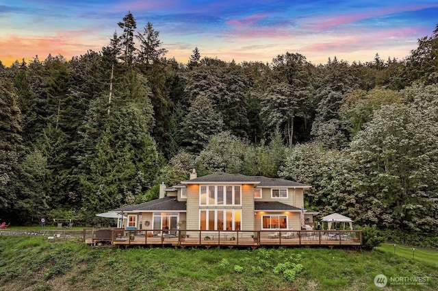 rear view of property with a wooded view, a yard, a chimney, and a deck