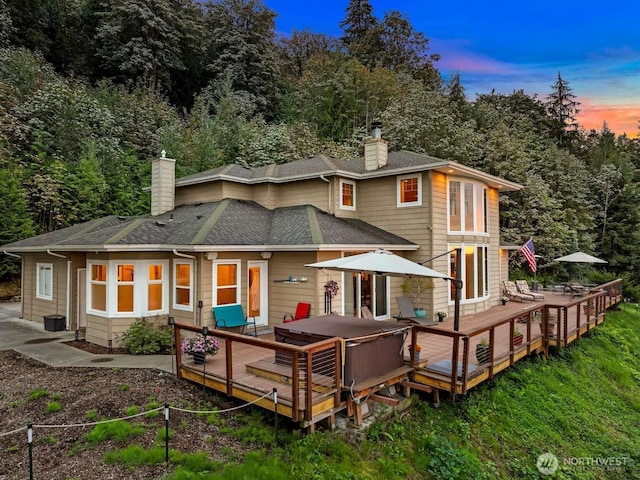 back of property with a shingled roof, a chimney, and a deck