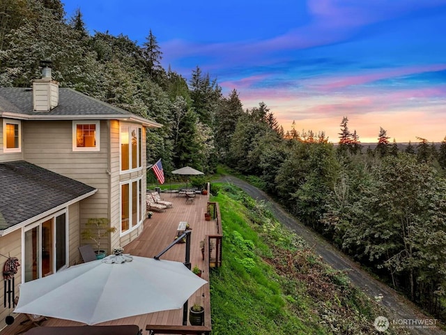 deck at dusk with a forest view and outdoor dining space