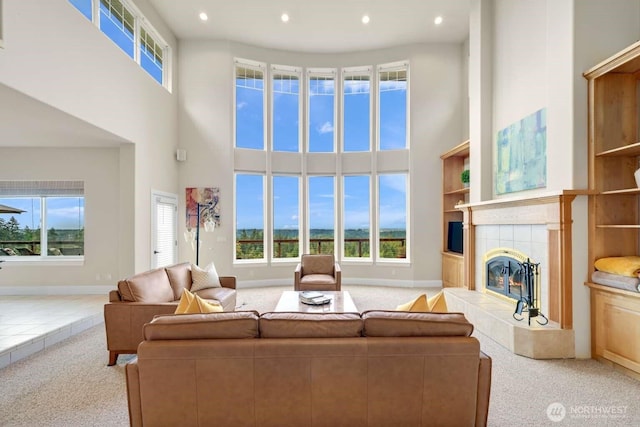 living area featuring carpet floors, a tile fireplace, a healthy amount of sunlight, and a towering ceiling
