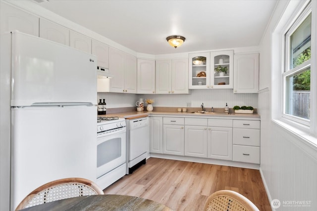 kitchen featuring white appliances, under cabinet range hood, light wood-style floors, a sink, and white cabinetry