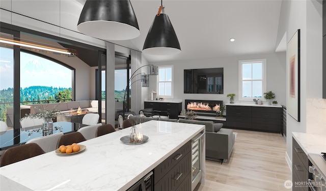 kitchen with light wood finished floors, light stone countertops, a wealth of natural light, and a glass covered fireplace