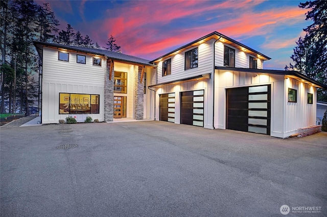 modern home with board and batten siding, an attached garage, driveway, and stone siding