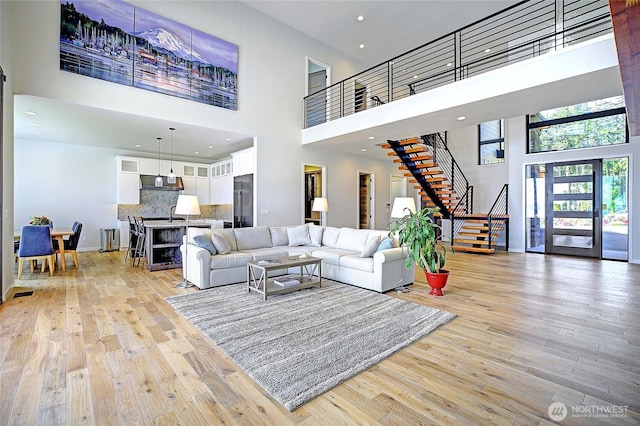 living area with recessed lighting, light wood-style flooring, a towering ceiling, and stairway