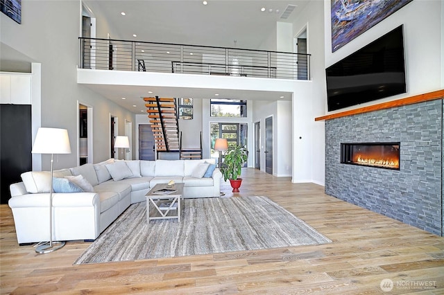 living room with visible vents, stairs, a glass covered fireplace, wood finished floors, and a high ceiling