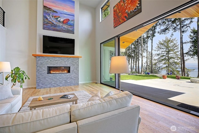 living area with wood finished floors, baseboards, a fireplace, and a towering ceiling