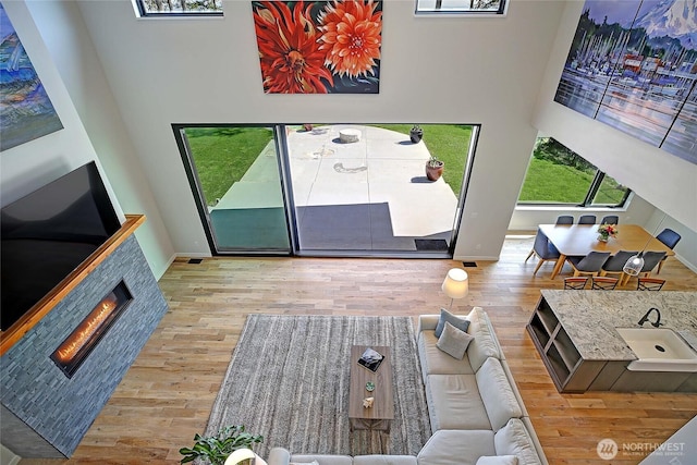 living area featuring a tiled fireplace, baseboards, a towering ceiling, and wood finished floors