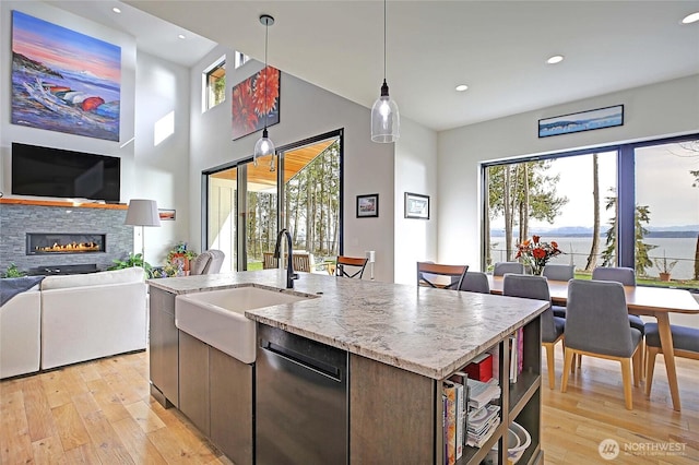 kitchen featuring a stone fireplace, a sink, light wood finished floors, open floor plan, and dishwashing machine