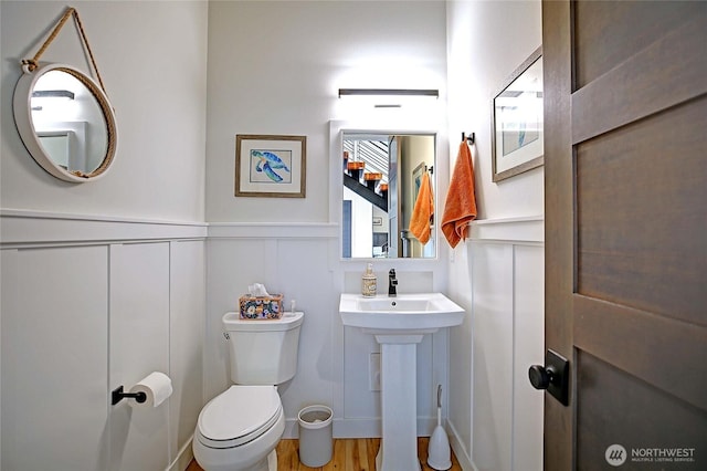 half bathroom featuring wood finished floors, wainscoting, a decorative wall, and toilet
