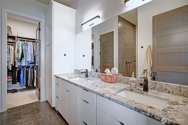 full bathroom with double vanity, a spacious closet, a shower stall, and a sink