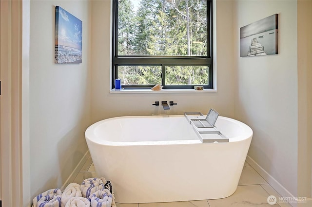 full bath featuring a freestanding tub, tile patterned flooring, and baseboards