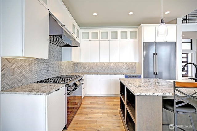1699 SE Camano Dr, Camano Island, WA 98282 - kitchen with appliances with stainless steel finishes, ventilation hood, light wood-style floors, a breakfast bar area, and pendant lighting