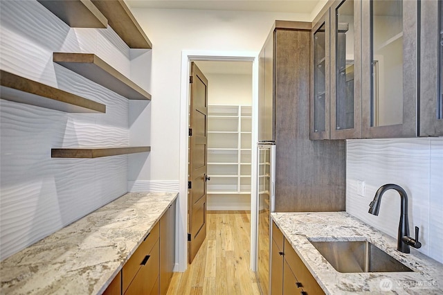 1699 SE Camano Dr, Camano Island, WA 98282 - kitchen featuring open shelves, light wood-type flooring, light stone counters, glass insert cabinets, and backsplash
