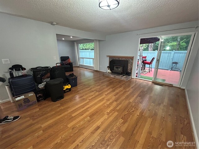 living area with wood finished floors, a textured ceiling, a fireplace with raised hearth, and baseboards