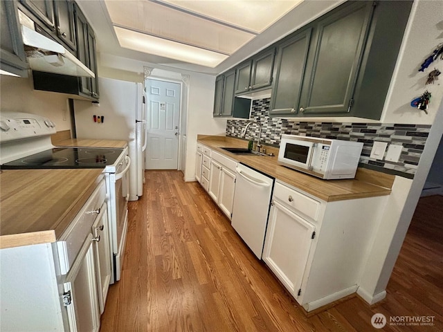 kitchen featuring white appliances, a sink, under cabinet range hood, and light wood finished floors