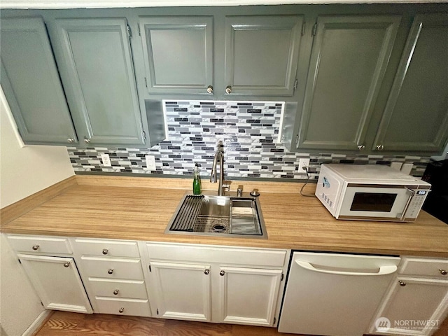 kitchen with a sink, light countertops, white microwave, dishwashing machine, and tasteful backsplash