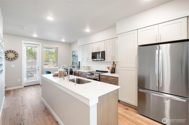 kitchen with a sink, light wood-style flooring, a center island with sink, and appliances with stainless steel finishes