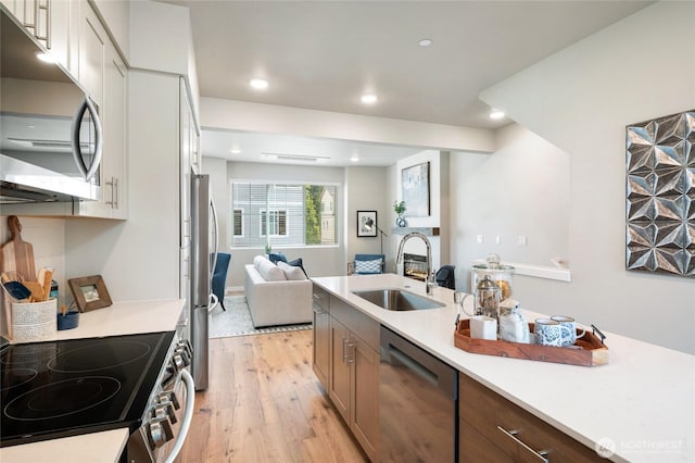 kitchen featuring a sink, light wood-type flooring, light countertops, open floor plan, and appliances with stainless steel finishes