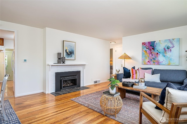 living room with wood finished floors, a brick fireplace, and baseboards