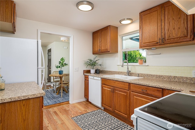 kitchen featuring white appliances, a sink, light wood finished floors, brown cabinets, and light countertops
