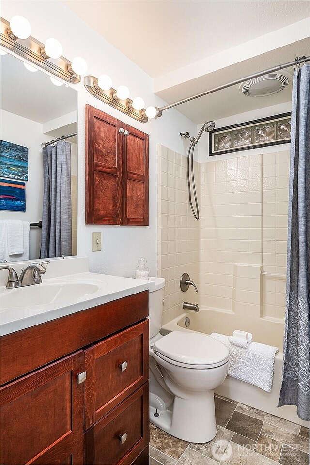 full bath featuring shower / bath combo, toilet, vanity, and stone tile floors