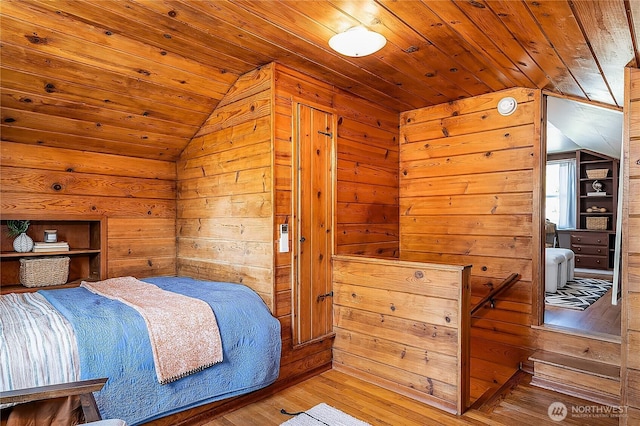 bedroom with vaulted ceiling, wood walls, and wood finished floors
