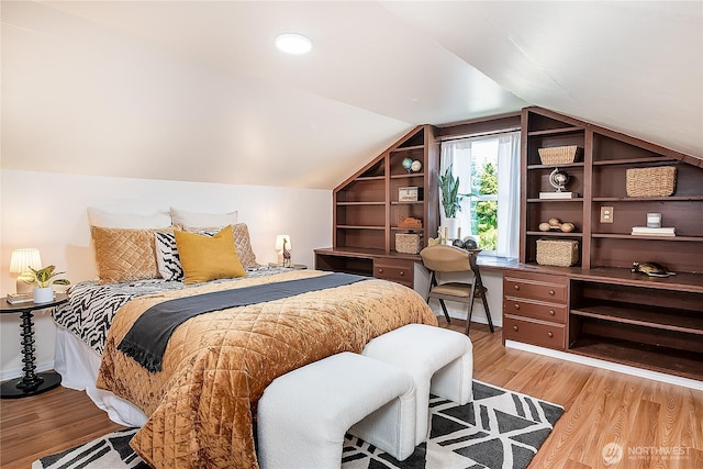 bedroom featuring light wood-style flooring, vaulted ceiling, and a desk