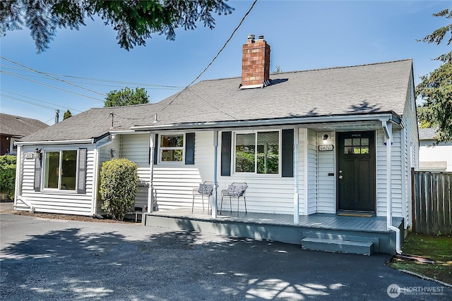 view of front of house featuring covered porch, a chimney, fence, and a shingled roof