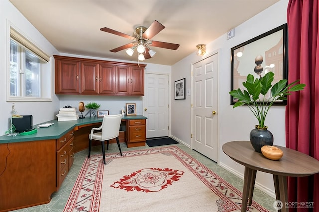 office area with built in desk, a ceiling fan, and baseboards
