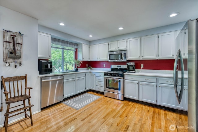 kitchen with appliances with stainless steel finishes, a sink, light countertops, light wood-type flooring, and recessed lighting