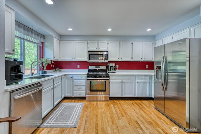 kitchen with appliances with stainless steel finishes, a sink, light countertops, white cabinetry, and light wood-style floors