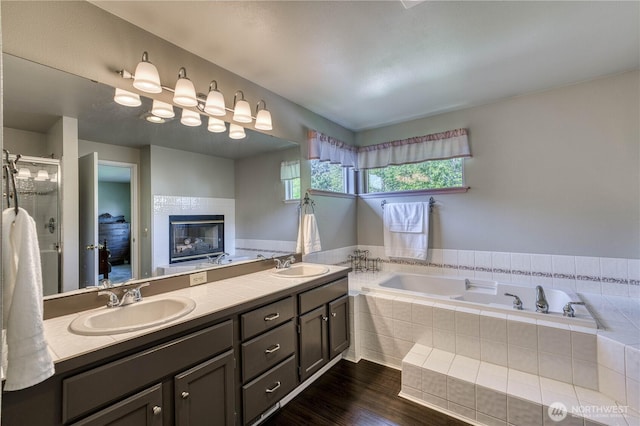 bathroom with a bath, double vanity, wood finished floors, a shower with shower door, and a fireplace