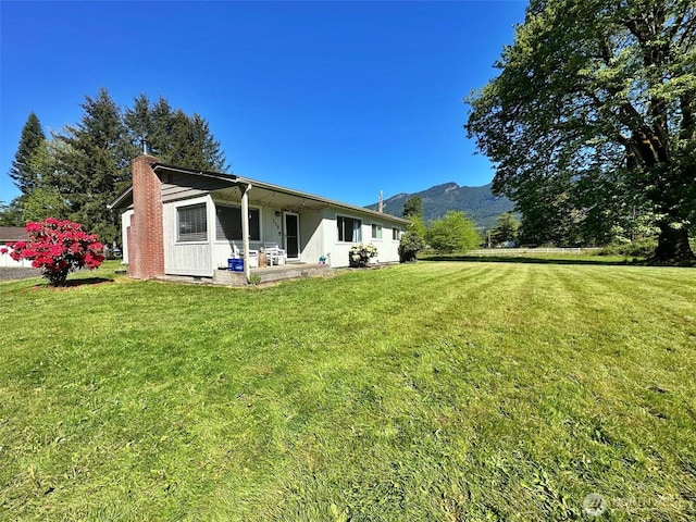 rear view of house featuring a chimney, a yard, and a mountain view