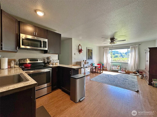 kitchen featuring appliances with stainless steel finishes, a peninsula, open floor plan, a textured ceiling, and light wood-type flooring