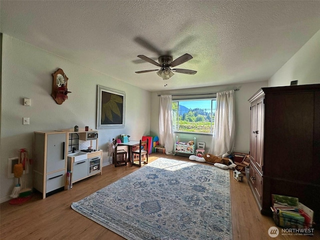 game room with a ceiling fan, wood finished floors, a textured ceiling, and baseboards