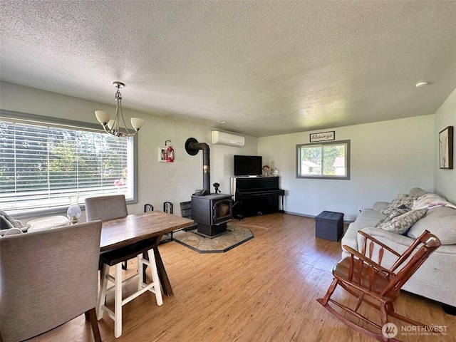 living area with a textured ceiling, a wood stove, a wall mounted AC, light wood-type flooring, and a chandelier