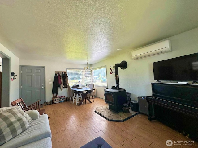living room with a wall mounted air conditioner, a textured ceiling, wood finished floors, a wood stove, and a chandelier