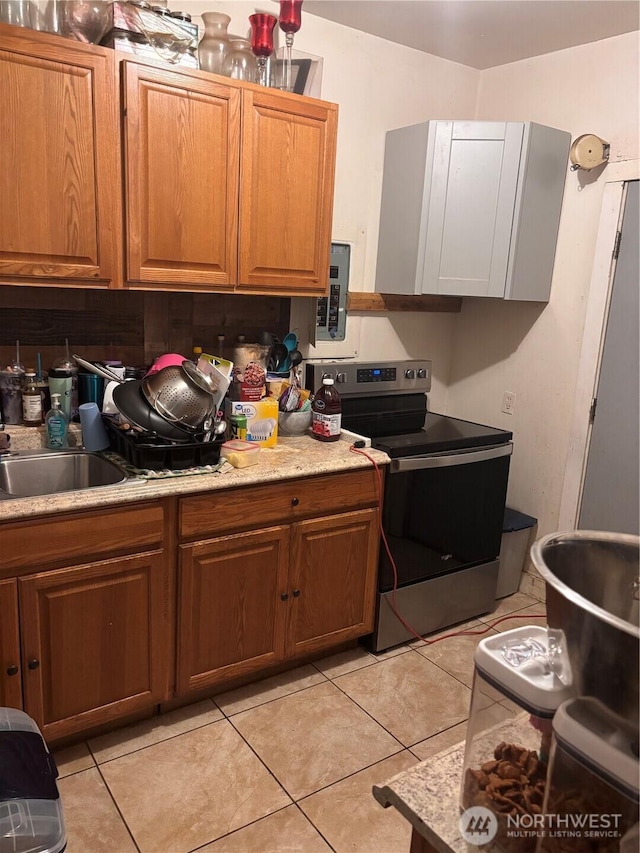kitchen featuring light tile patterned floors, brown cabinets, light countertops, and stainless steel electric range