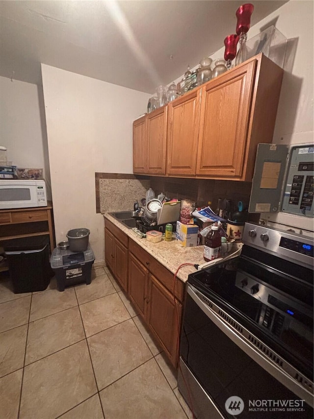 kitchen with stainless steel range with electric stovetop, a sink, white microwave, light countertops, and light tile patterned flooring