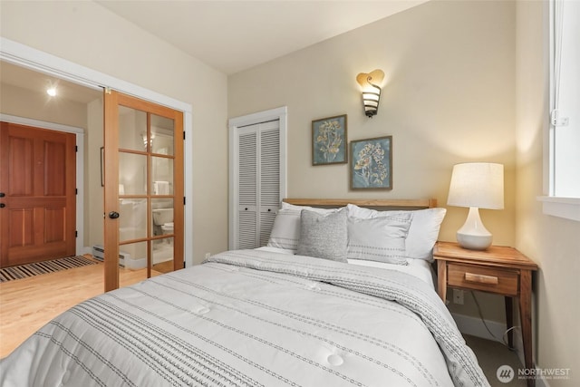 bedroom with wood finished floors, a closet, and baseboard heating