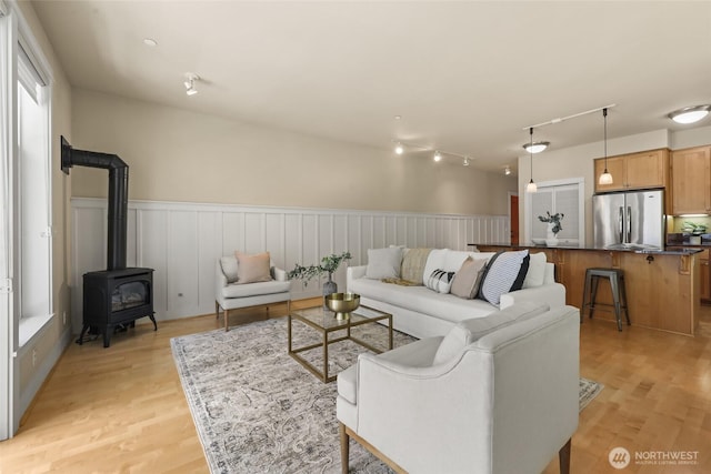 living room with a wood stove, a wainscoted wall, light wood-style flooring, and track lighting