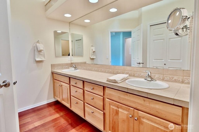 full bathroom featuring a sink, double vanity, baseboards, and wood finished floors