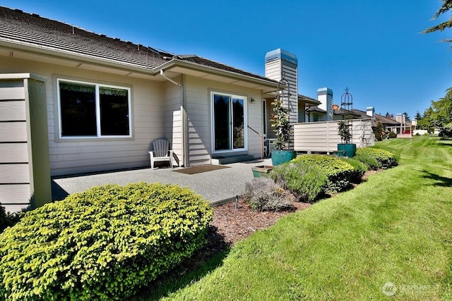 rear view of house featuring a patio area, a chimney, and a lawn