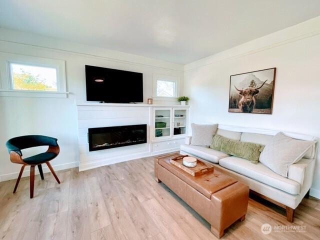 living room featuring wood finished floors, a glass covered fireplace, and baseboards